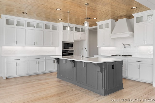 kitchen featuring wall oven, premium range hood, a sink, wood ceiling, and stainless steel microwave