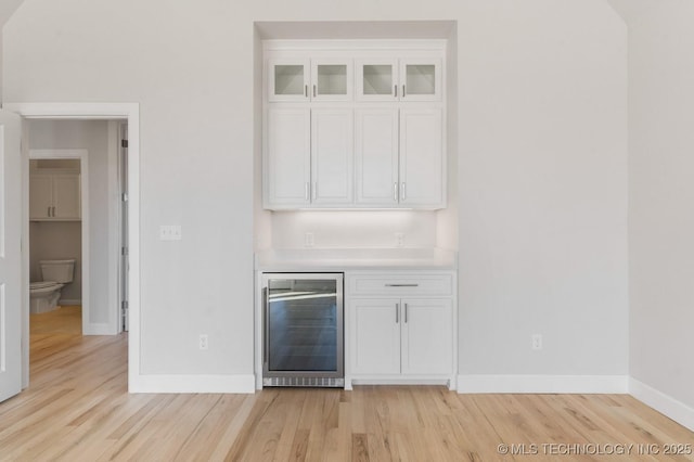 bar with a dry bar, light wood finished floors, and beverage cooler