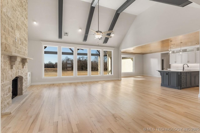 unfurnished living room featuring visible vents, light wood-style flooring, a sink, a fireplace, and beam ceiling