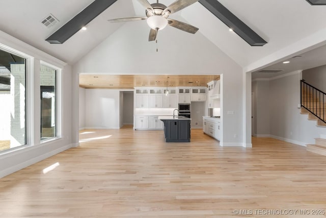 unfurnished living room featuring a ceiling fan, baseboards, visible vents, light wood-style floors, and stairway