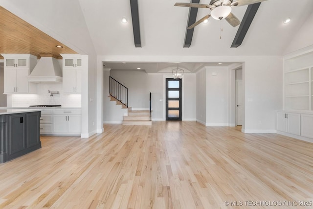 unfurnished living room featuring light wood finished floors, stairway, beam ceiling, and baseboards