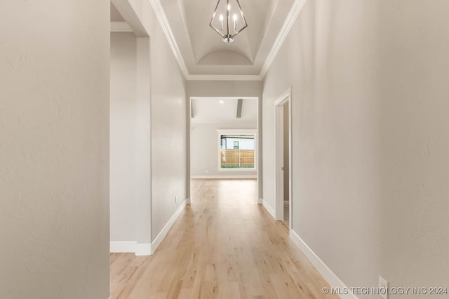 corridor featuring a raised ceiling, a notable chandelier, ornamental molding, and light hardwood / wood-style flooring