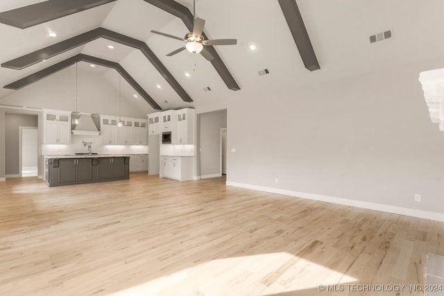 unfurnished living room featuring high vaulted ceiling, sink, light hardwood / wood-style floors, and beam ceiling