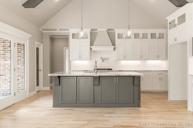 kitchen with custom exhaust hood, a wealth of natural light, a center island with sink, and white cabinets