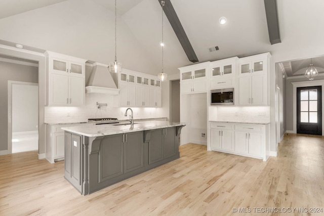 kitchen featuring white cabinets, light hardwood / wood-style flooring, beamed ceiling, and an island with sink