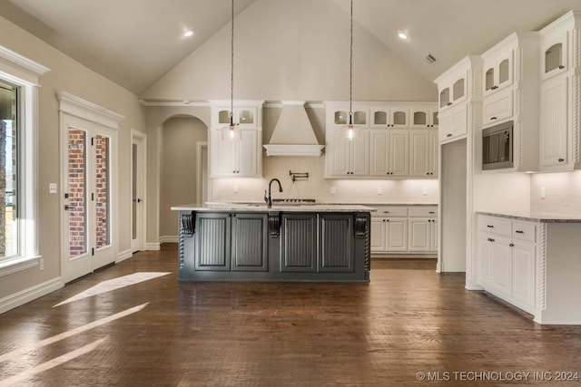 kitchen with hanging light fixtures, high vaulted ceiling, a kitchen island with sink, white cabinets, and custom exhaust hood