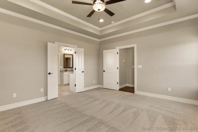 unfurnished bedroom featuring ceiling fan, a raised ceiling, ensuite bathroom, light carpet, and ornamental molding