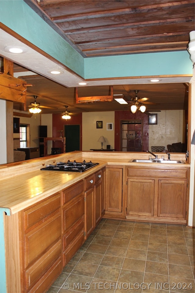 kitchen featuring black gas cooktop, tile flooring, ceiling fan, beamed ceiling, and sink