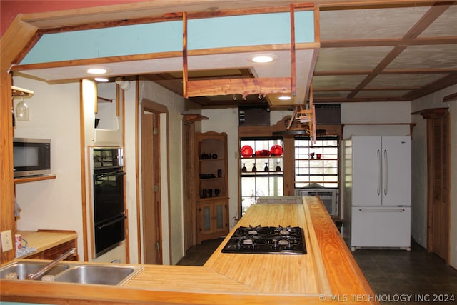 kitchen featuring sink, dark tile floors, butcher block counters, and black appliances