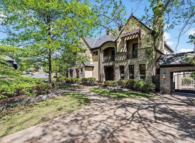 tudor home featuring stone siding, a balcony, driveway, and stucco siding