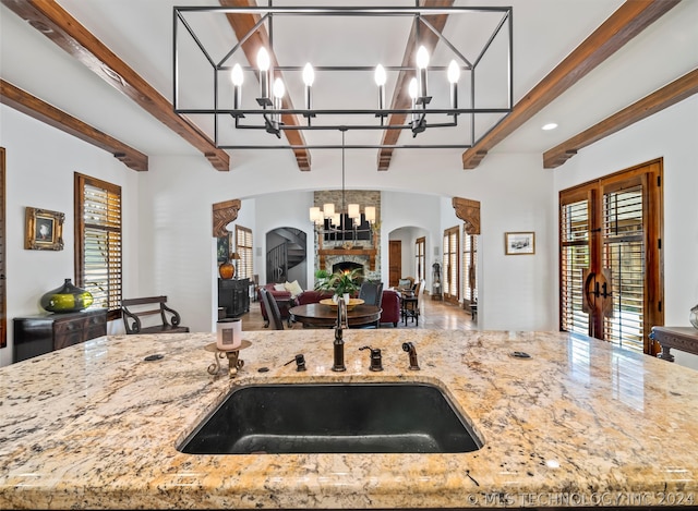 kitchen with hanging light fixtures, light stone countertops, a fireplace, and beamed ceiling