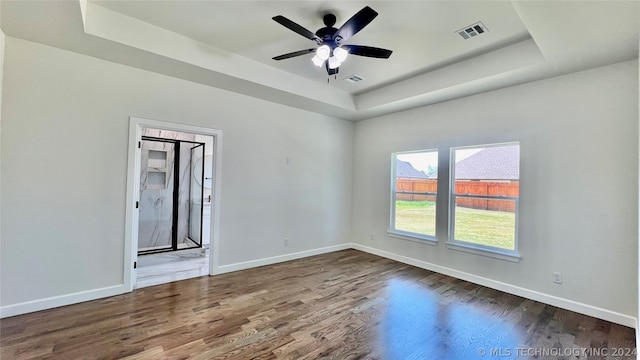 spare room with dark hardwood / wood-style floors, ceiling fan, and a raised ceiling