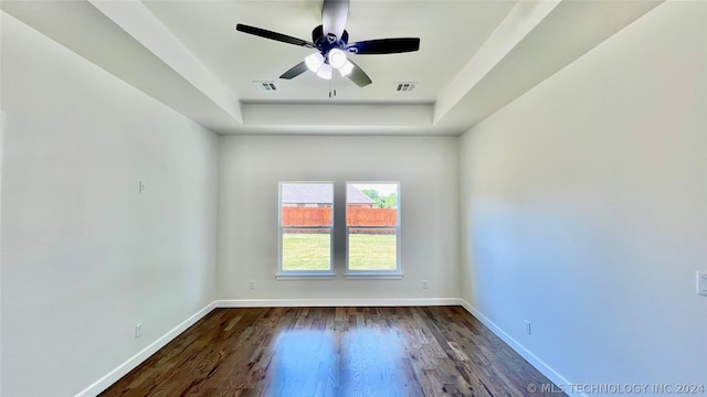 empty room with dark wood-type flooring, ceiling fan, and a raised ceiling