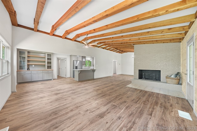 unfurnished living room featuring ceiling fan, light hardwood / wood-style flooring, beamed ceiling, a fireplace, and brick wall