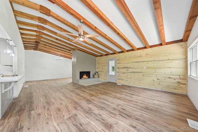 unfurnished living room with hardwood / wood-style floors, wooden walls, lofted ceiling with beams, and a large fireplace