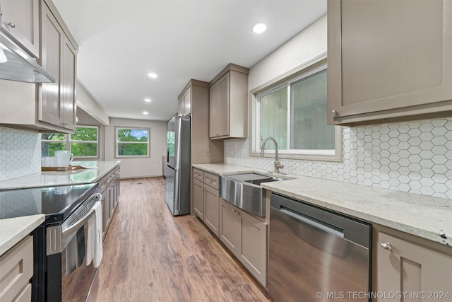 kitchen featuring light stone counters, backsplash, hardwood / wood-style floors, appliances with stainless steel finishes, and sink