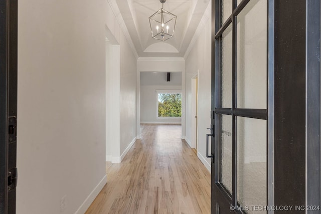 corridor featuring a raised ceiling, light wood-type flooring, crown molding, and a chandelier