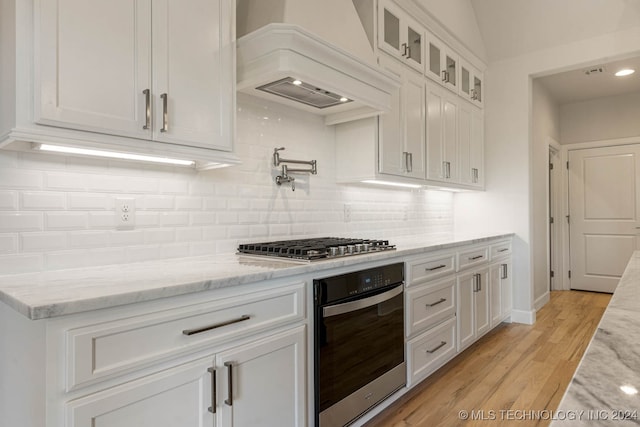 kitchen with white cabinetry, light stone counters, premium range hood, light hardwood / wood-style floors, and appliances with stainless steel finishes