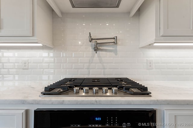 details featuring tasteful backsplash, light stone counters, white cabinets, and stainless steel gas cooktop