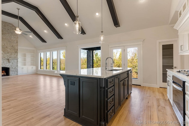 kitchen with a fireplace, a kitchen island with sink, sink, and beamed ceiling