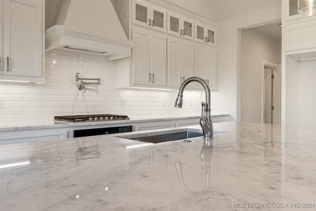 kitchen with white cabinets, sink, light stone countertops, custom range hood, and stainless steel gas cooktop