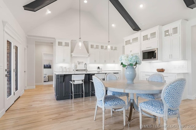 dining area with high vaulted ceiling, sink, and light wood-type flooring