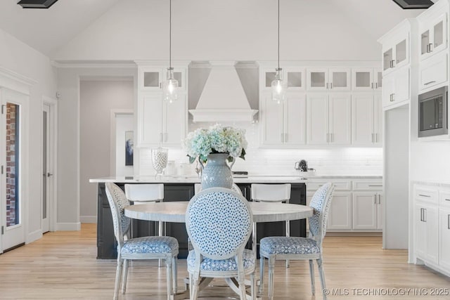 kitchen with pendant lighting, lofted ceiling, stainless steel microwave, white cabinets, and custom exhaust hood