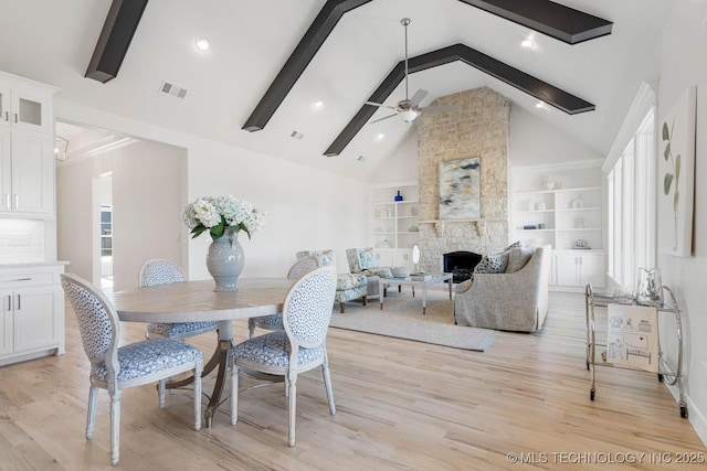 dining room featuring ceiling fan, beam ceiling, high vaulted ceiling, a fireplace, and light wood-type flooring