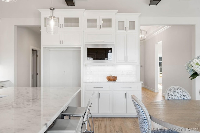 kitchen with hanging light fixtures, light stone countertops, light hardwood / wood-style floors, and white cabinets