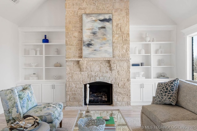 living room with vaulted ceiling, a stone fireplace, built in features, and light hardwood / wood-style floors