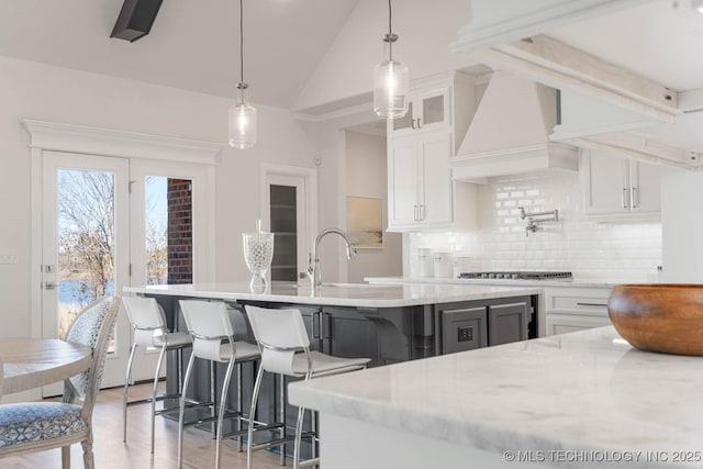 kitchen with lofted ceiling, sink, custom exhaust hood, white cabinetry, and pendant lighting