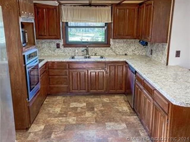 kitchen featuring kitchen peninsula, backsplash, appliances with stainless steel finishes, sink, and light tile floors