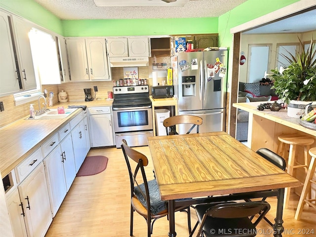 kitchen featuring stainless steel appliances, light wood-type flooring, a textured ceiling, backsplash, and white cabinetry