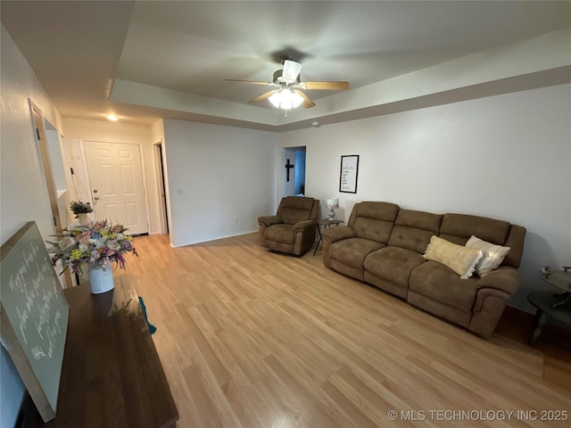 living room featuring ceiling fan, a tray ceiling, and light wood-type flooring