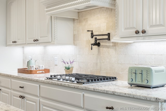 kitchen featuring light stone counters, white cabinetry, tasteful backsplash, and stainless steel gas cooktop