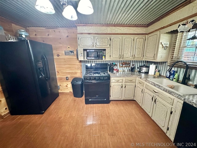 kitchen featuring light hardwood / wood-style flooring, wood walls, black appliances, ornamental molding, and sink