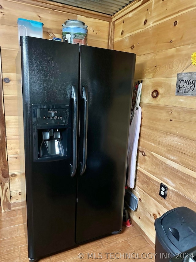 room details with wood walls, light wood-type flooring, and black refrigerator with ice dispenser