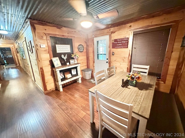 dining space with wood-type flooring, ceiling fan, and wood walls