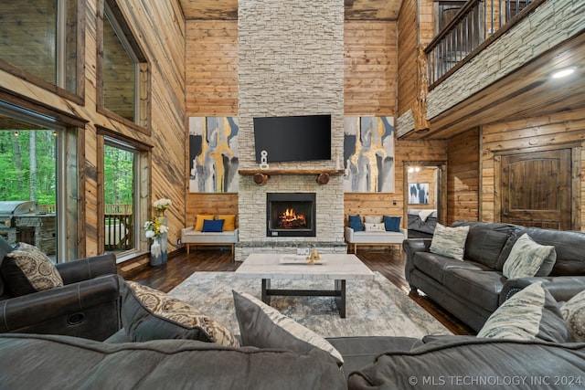 living room featuring a stone fireplace, wooden walls, a high ceiling, and dark hardwood / wood-style floors