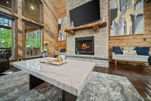 living room with wooden walls, a towering ceiling, a stone fireplace, and dark wood-type flooring