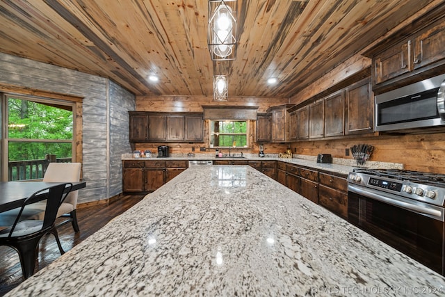 kitchen featuring light stone countertops, dark wood-type flooring, appliances with stainless steel finishes, pendant lighting, and sink