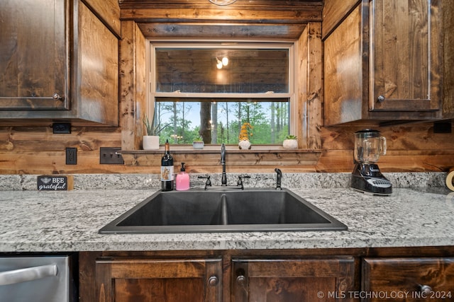 kitchen featuring wooden walls, sink, dishwasher, and light stone counters