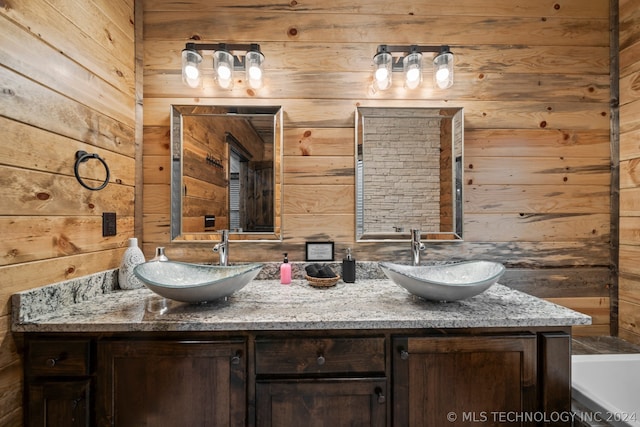 bathroom featuring a bath, wood walls, and dual bowl vanity