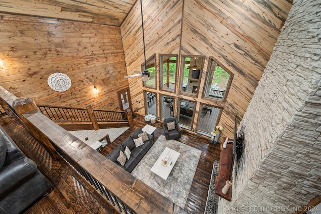 unfurnished living room with high vaulted ceiling, wood-type flooring, wooden walls, and ceiling fan