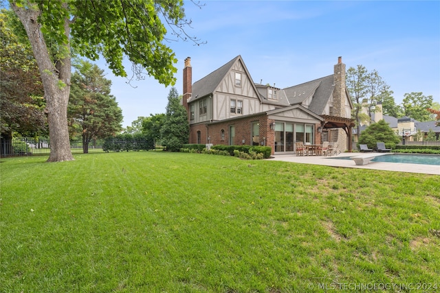 tudor-style house with a patio, a front lawn, and a fenced in pool