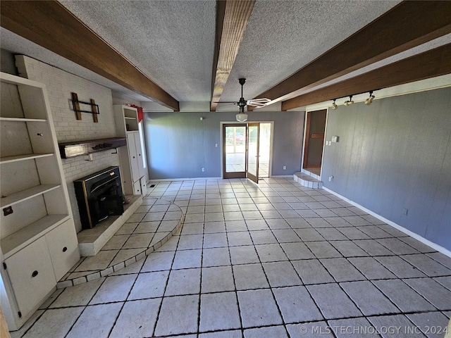 unfurnished living room with a wood stove, ceiling fan, beamed ceiling, a textured ceiling, and light tile patterned floors