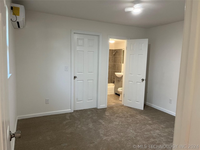 unfurnished bedroom with an AC wall unit, ensuite bath, and dark colored carpet