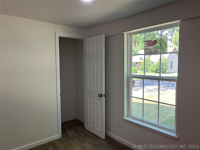 unfurnished bedroom featuring multiple windows, a closet, and dark colored carpet