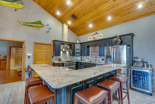 kitchen featuring wall chimney range hood, backsplash, a breakfast bar area, high vaulted ceiling, and appliances with stainless steel finishes