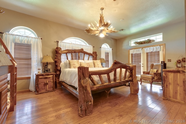 bedroom featuring french doors, a textured ceiling, light wood-type flooring, and a chandelier